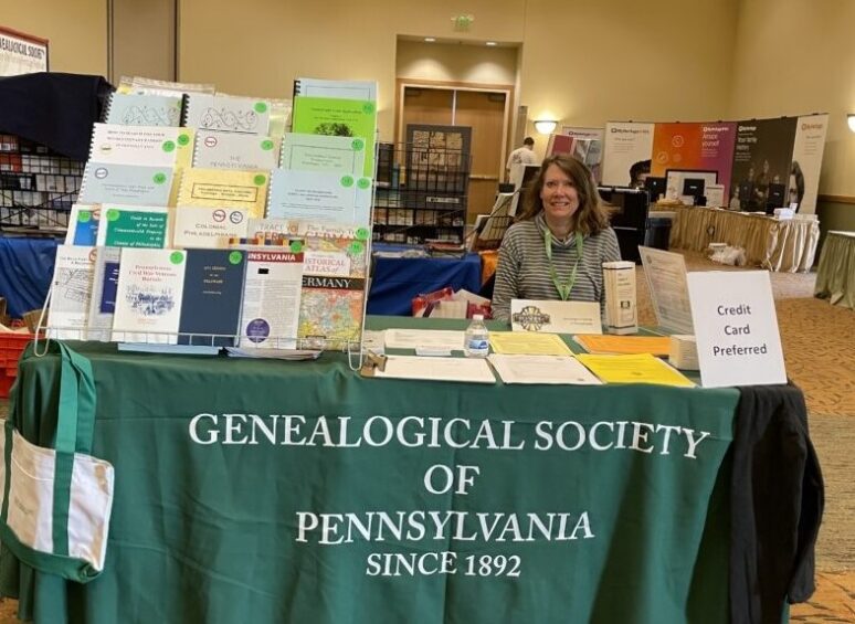 Vendor table at conference with publications for sale and smiling woman seated at table